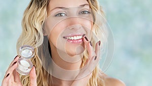 Beautiful smiling girl with wavy hair using lip balm or gloss.  Young blonde woman applying make-up cosmetic SPA product