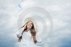 Beautiful smiling girl in a white hat with a wide brim talking on the phone on background of storm clouds