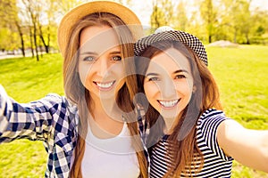 Beautiful smiling girls in hats making selfie in the park