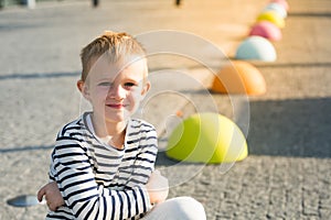 Beautiful smiling happy little boy sit on colored stones, looking at camera