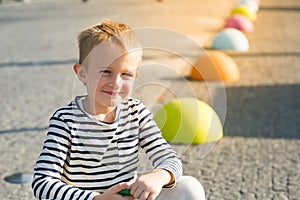 Beautiful smiling happy little boy sitting on colored stones, looking at camera