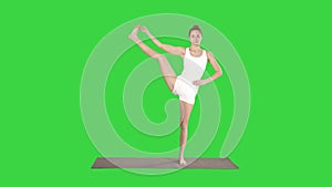 Beautiful smiling happy young woman doing yoga exercise on mat, standing in Vrksasana Posture, Tree Pose on a Green