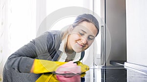 Beautiful smiling housewife cleaning stained glas surface of electric hob