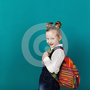 Beautiful smiling little girl with big backpack standing against