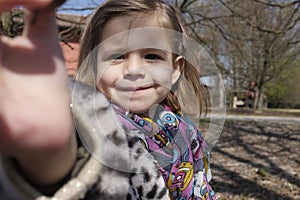 Beautiful smiling little girl closeup on background of city park in autumn. Leopard-print fur coat. Looking at camera