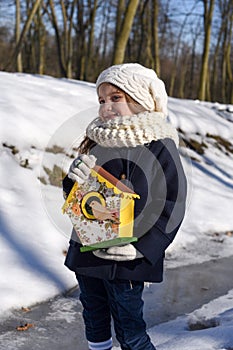 A beautiful smiling little girl holding a bird house in a park