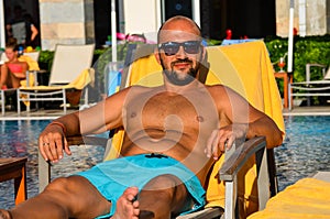 Beautiful smiling Man with sunglasses and wedding ring relaxing and lazing at pool and having a good time