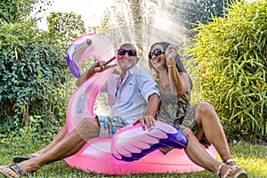 beautiful smiling middle aged couple sitting on pink flamingo inflatable toy
