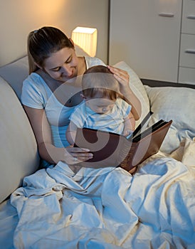 Beautiful smiling mother reading story to her baby boy before go