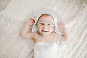 Beautiful smiling newborn baby boy covered with white bamboo towel with fun ears. Sitting on a white knit, wool plaid bright inter