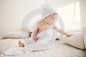 Beautiful smiling newborn baby boy covered with white bamboo towel with fun ears. Sitting on a white knit, wool plaid bright inter