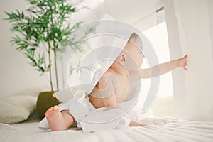 Beautiful smiling newborn baby boy covered with white bamboo towel with fun ears. Sitting on a white knit, wool plaid bright inter