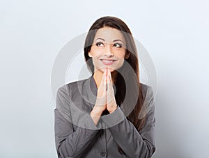 Beautiful smiling praying business woman in office clothing gesturing the hands the plea sign and looking up on blue background.