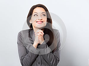 Beautiful smiling praying business woman in office clothing gesturing the hands the plea sign and looking up on blue background.