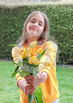 Beautiful smiling preteen girl giving bouquet of spring yellow tulips looking at camera.