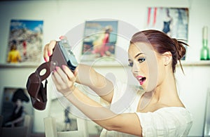 Beautiful, smiling red hair woman taking photos of herself with a camera. Fashionable attractive female taking a self portrait