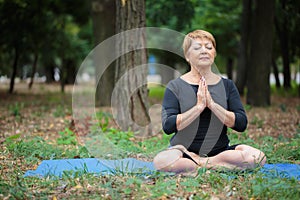 Beautiful, smiling senior woman in a lotus position on a park background. Meditation concept. Copy space.