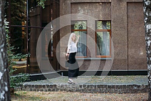 A beautiful smiling slender woman with long blond hair walks along the city street