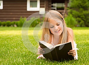 Beautiful smiling teenage girl lying on grass and read book