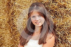 Beautiful smiling teenage girl sitting near a hay bale