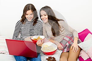 Beautiful smiling teenage girls watching movies on notebook