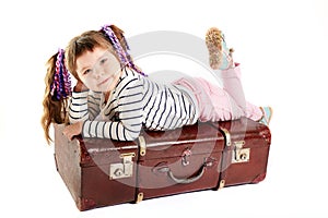 Beautiful smiling toddler girl laying on retro suitcase