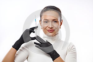 Beautiful smiling woman in black gloves holding a syringe near her face. Concept of injection cosmetology and anti-aging therapy