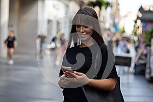 Beautiful smiling woman in black shirt texting on smartphone on street
