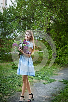 Beautiful woman in a blue summer dress with lilac flowers in a blooming garden. Spring Blossom