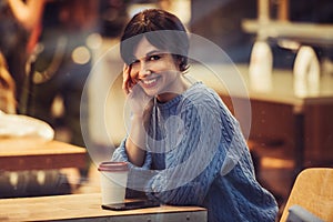 Beautiful smiling woman in the cafe with warm cozy interior and drinking coffee