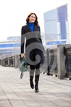 Beautiful smiling woman in dark coat with handbag and laptop