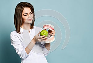 Beautiful smiling woman dentist or doctor orthodontist holding artificial jaw and fresh green apple and showing healthy teeth