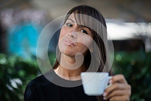 Beautiful smiling woman drinking coffee in garden of cafe