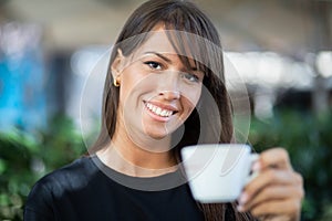 Beautiful smiling woman drinking coffee in garden of cafe