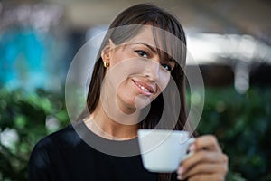 Beautiful smiling woman drinking coffee in garden of cafe