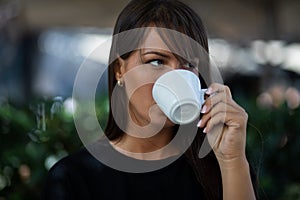 Beautiful smiling woman drinking coffee in garden of cafe