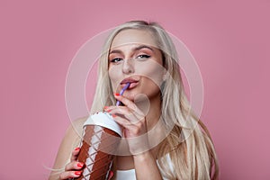 Beautiful smiling blond woman drinking ice cream cocktail over pink background