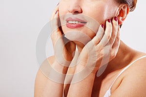 Beautiful smiling woman face close up . Anti age concept. Collagen and plastic surgery. Female touching her face. Red mani