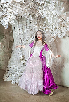 Beautiful smiling woman in fantasy white and purple rococo style medieval dress standing near tree with white flowers