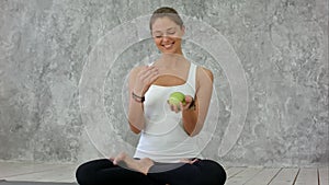 Beautiful smiling woman holding green apple, jungle with it, sitting in lotus pose