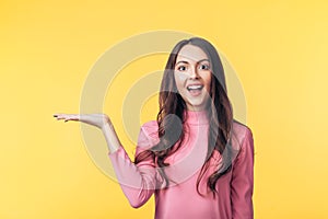 Beautiful smiling woman holding and presenting copy space on her palm isolated on yellow background