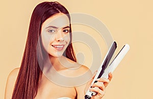 Beautiful smiling woman ironing long hair with flat iron. Woman straightening hair with straightener. Portrait of young