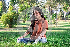 Beautiful smiling woman with long African braids is doing yoga outside in a park. Concept of healthy lifestyle
