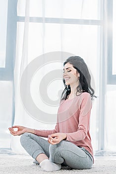 Beautiful smiling woman in Lotus Pose practicing meditation in Living Room at home.