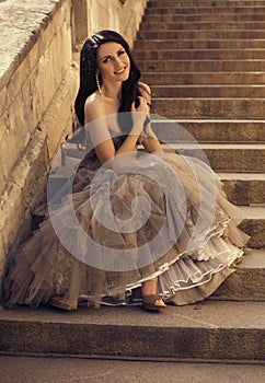 Beautiful smiling woman in luxurious dress sitting on stairs