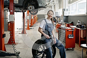 Beautiful smiling woman mechanic sitting on wheel at tire replacement service