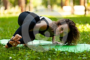 Beautiful smiling woman in morning park doing yoga and outdoor gymnastics. Green grass and rays of sun