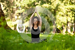 Beautiful smiling woman in morning park doing yoga and outdoor gymnastics. Green grass and rays of sun