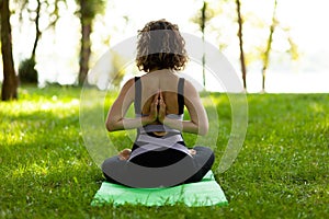 Beautiful smiling woman in morning park doing yoga and outdoor gymnastics. Green grass and rays of sun