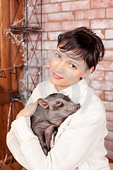Beautiful smiling woman near a Christmas tree holding in hands black vietnamese piglet. Concept of the Chinese New Year